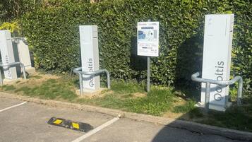 Estaciones de carga para vehículos eléctricos con barandillas metálicas, identificadas con 'Povoltis', sobre un fondo de follaje verde.