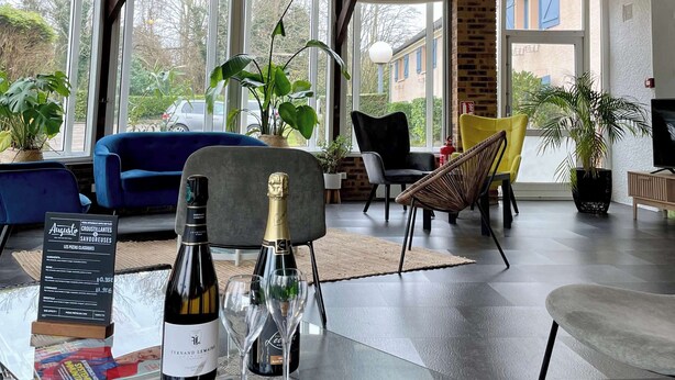 A spacious living area with large windows, wicker pendant lights, and a variety of seating options including a blue sofa and chairs. - Kyriad Epernay (Epernay)