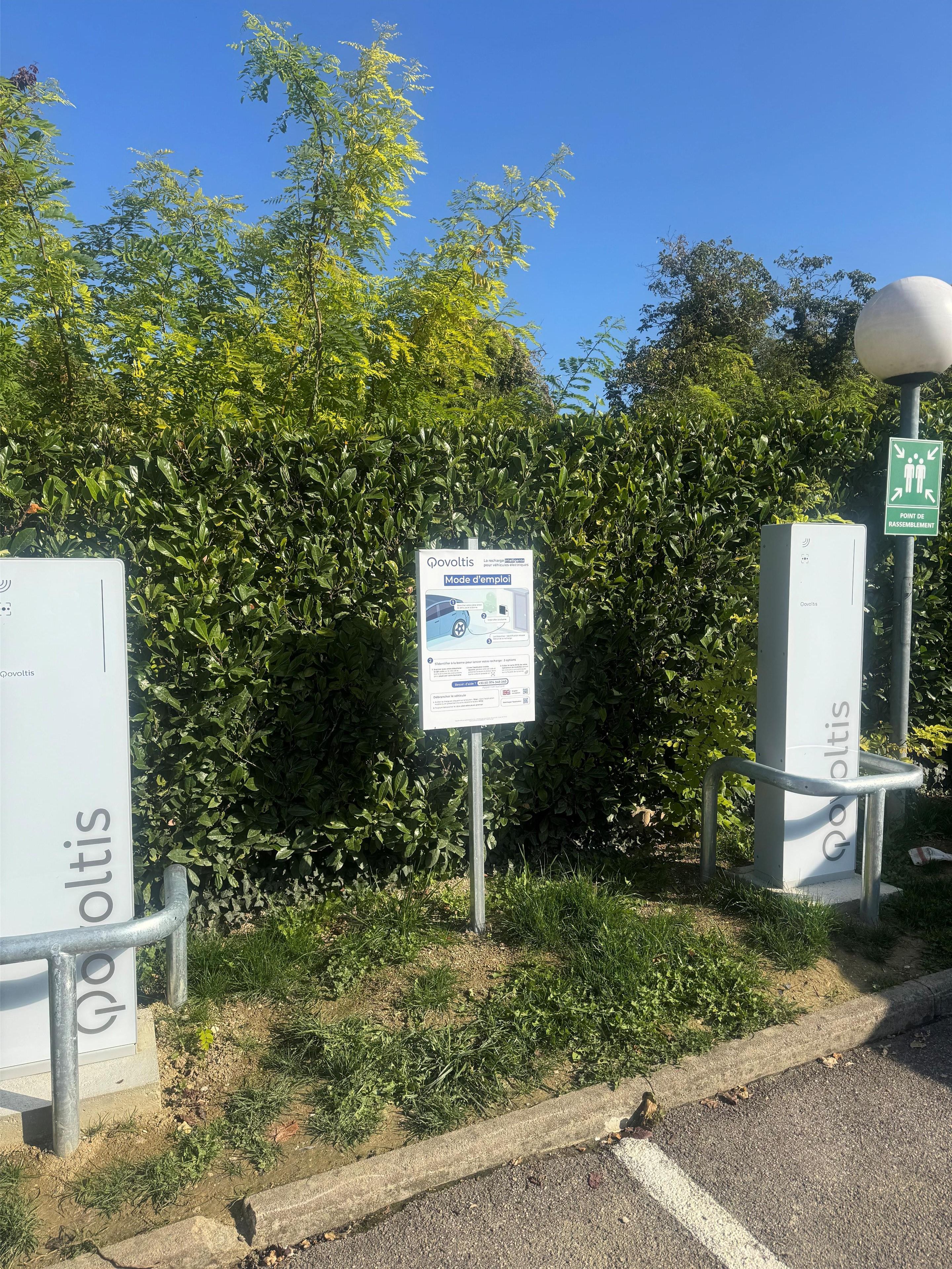Un cartel con información sobre un área de estacionamiento, rodeado de vegetación y cielo despejado.