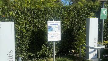 Un cartel con información sobre un área de estacionamiento, rodeado de vegetación y cielo despejado.