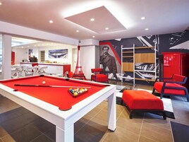 Una mesa de billar con superficie de fieltro rojo, una silla roja y un otoman rojo.
