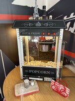 Una máquina de palomitas de maíz con cubierta de vidrio, un recipiente metálico en su interior y una pequeña bandeja de metal con una bolsa de palomitas y saleros.