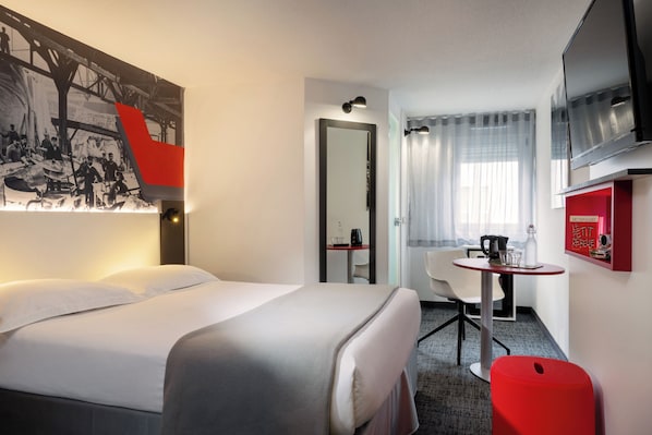 Une chambre d’hôtel avec un lit, un bureau, une chaise, une télévision et un meuble rouge.