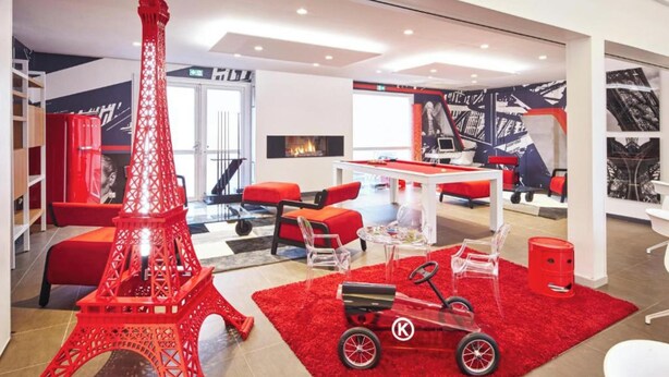 A modern hotel lobby with a large Eiffel Tower model, red seating, a pool table, and a fireplace.