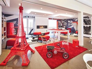 A modern hotel lobby with a large Eiffel Tower model, red seating, a pool table, and a fireplace. - Hôtel Gustave Colmar (Colmar)