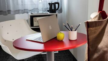 A modern hotel room with a red table, a laptop, an apple, and a cup with pencils.