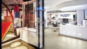 An office space with a modern design, featuring a reception area with a counter and chairs, and a visible staircase with a unique metal structure.