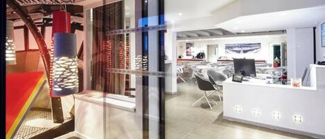 An office space with a modern design, featuring a reception area with a counter and chairs, and a visible staircase with a unique metal structure.