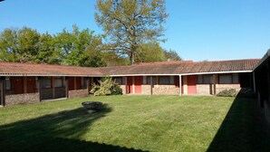 A motel with a red exterior, multiple rooms, and a small lawn area with a fire pit.