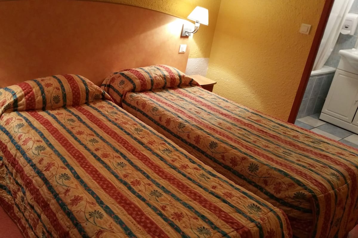 Cama de casal com roupa de cama estampada em um quarto com cabeceira de madeira e duas luminárias fixadas na parede.