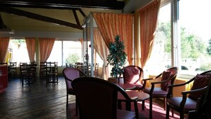 A room with wooden floors, a large window with orange curtains, and several chairs and tables.