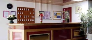 Uma mesa de recepção com um mural de avisos, obras de arte emolduradas e um vaso de plantas.