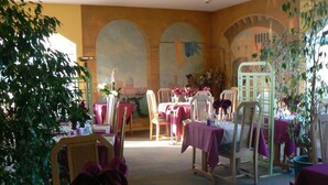 Un espace repas avec des tables dressées pour les invités, des chaises et une grande plante.