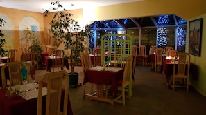Restaurante com várias mesas, cadeiras e plantas em vasos.