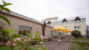 Un bâtiment doté d’un toit plat, de grandes fenêtres et d’une cour pavée agrémentée de parasols jaunes.