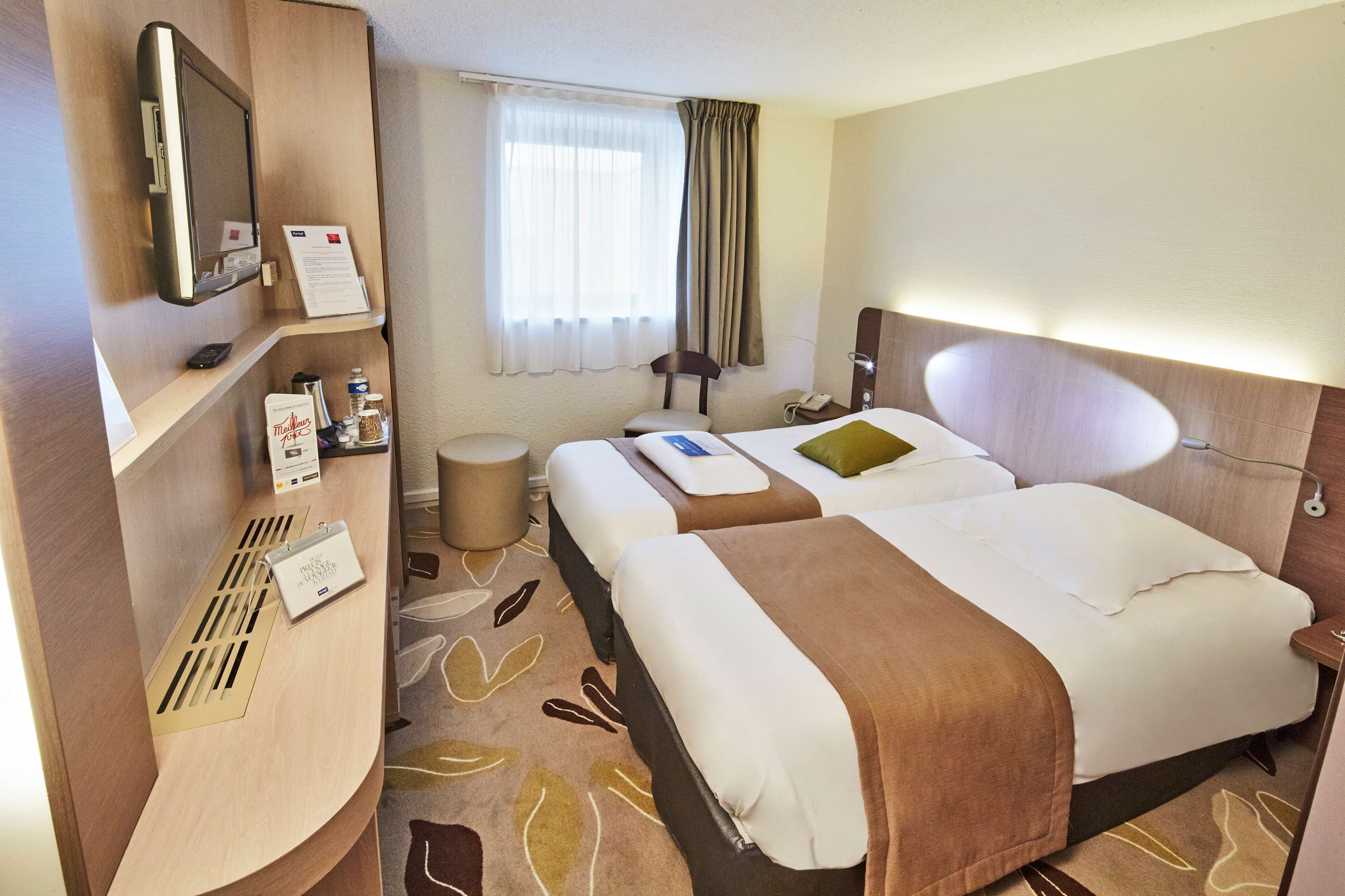 Habitación de hotel con dos camas, un escritorio con computadora, teléfono y ventana con cortinas.