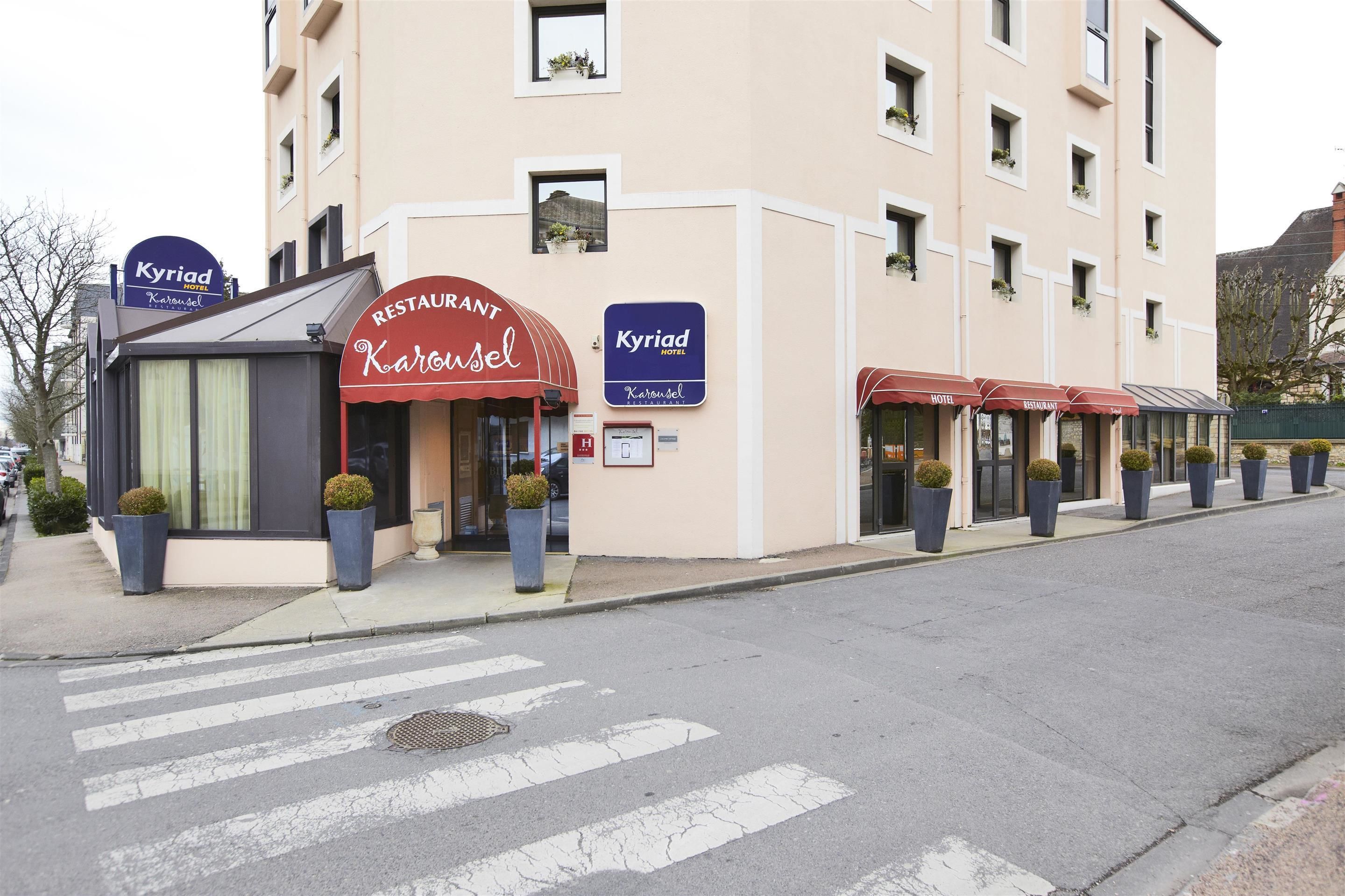 Un hotel con restaurante llamado Karossel, que tiene un toldo rojo y plantas en macetas.