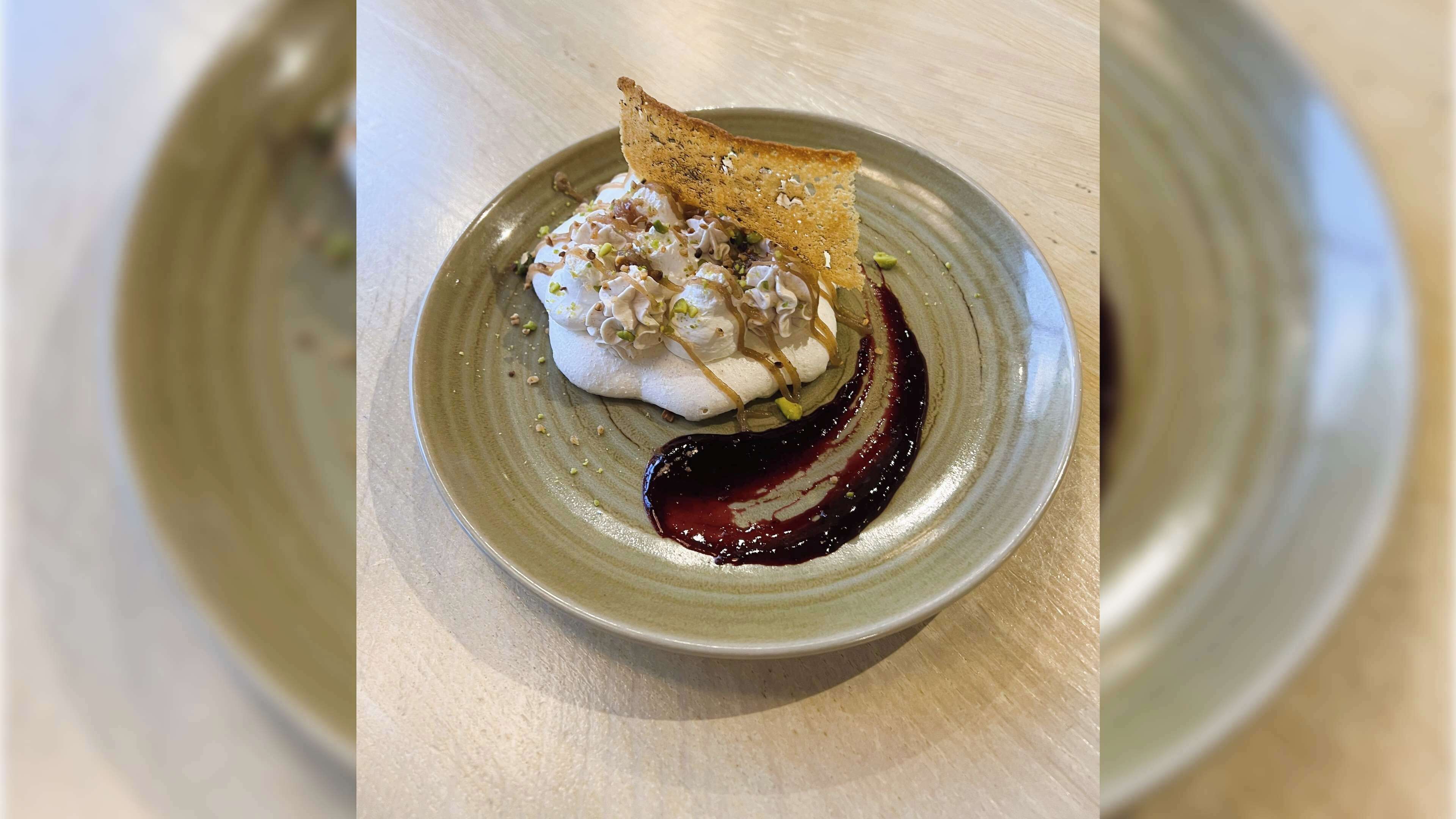 Ein Dessert auf einem Keramikteller mit Schlagsahne und einem Zuckerguss, dazu eine Scheibe Toast.