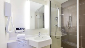 A modern bathroom with a white sink, mirror, and glass-enclosed shower.