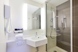 A modern bathroom with a white sink, mirror, and glass-enclosed shower.