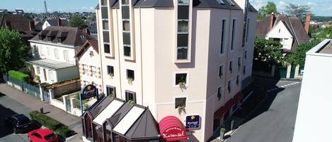 A multi-story building with a restaurant named 'Kyria Restaurant Karusel' on the ground floor. There are several cars parked on the street in front.