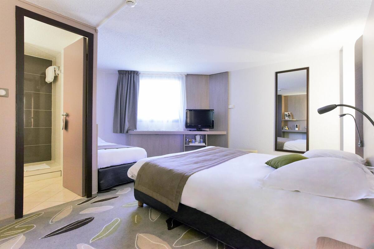A hotel room with two beds, a bathroom, a TV, and a mirror.