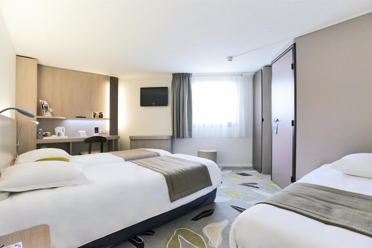 A hotel room with two beds, a desk with a chair, a TV, and a window with curtains.