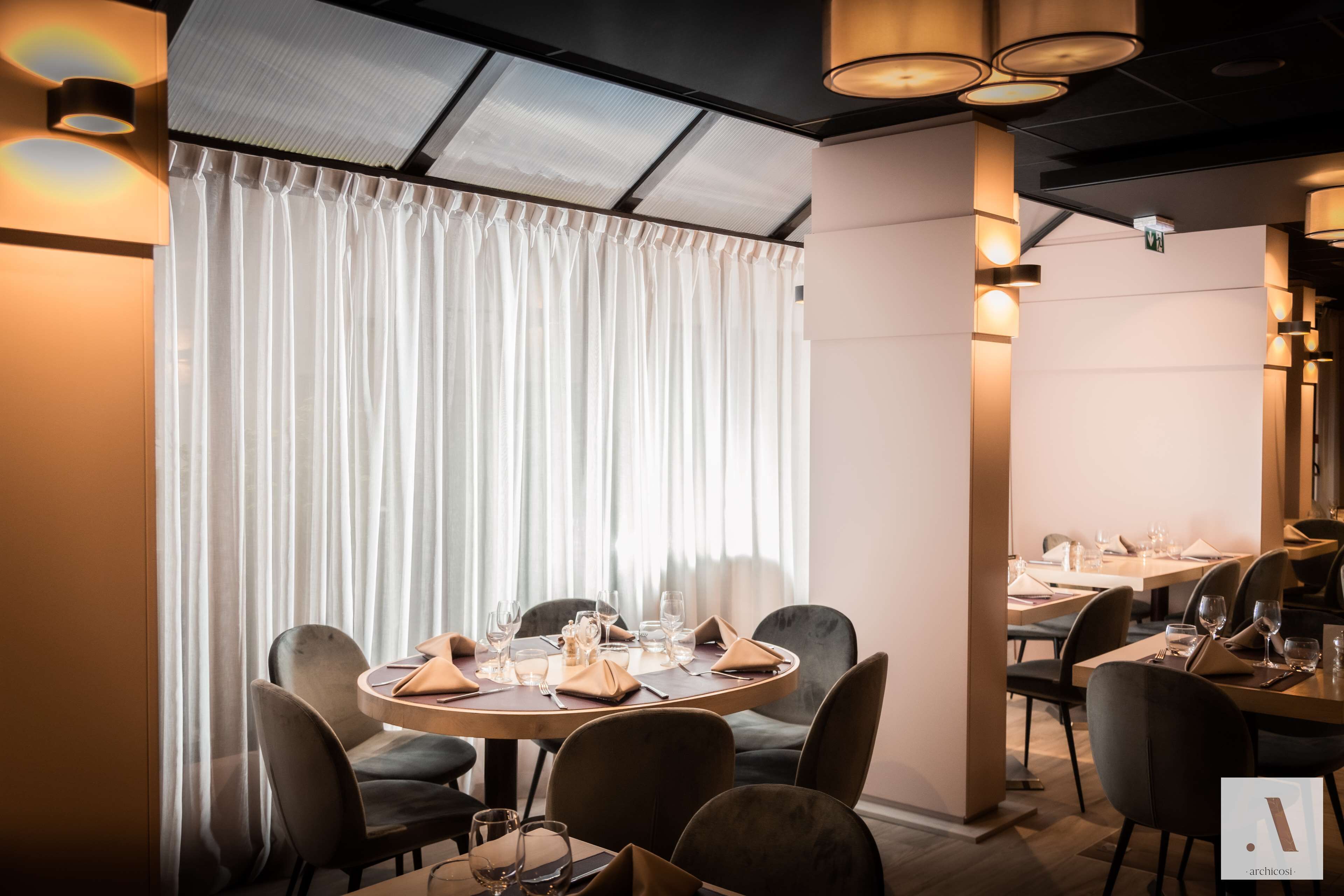 A dining area with round tables, chairs, and a large window with curtains.