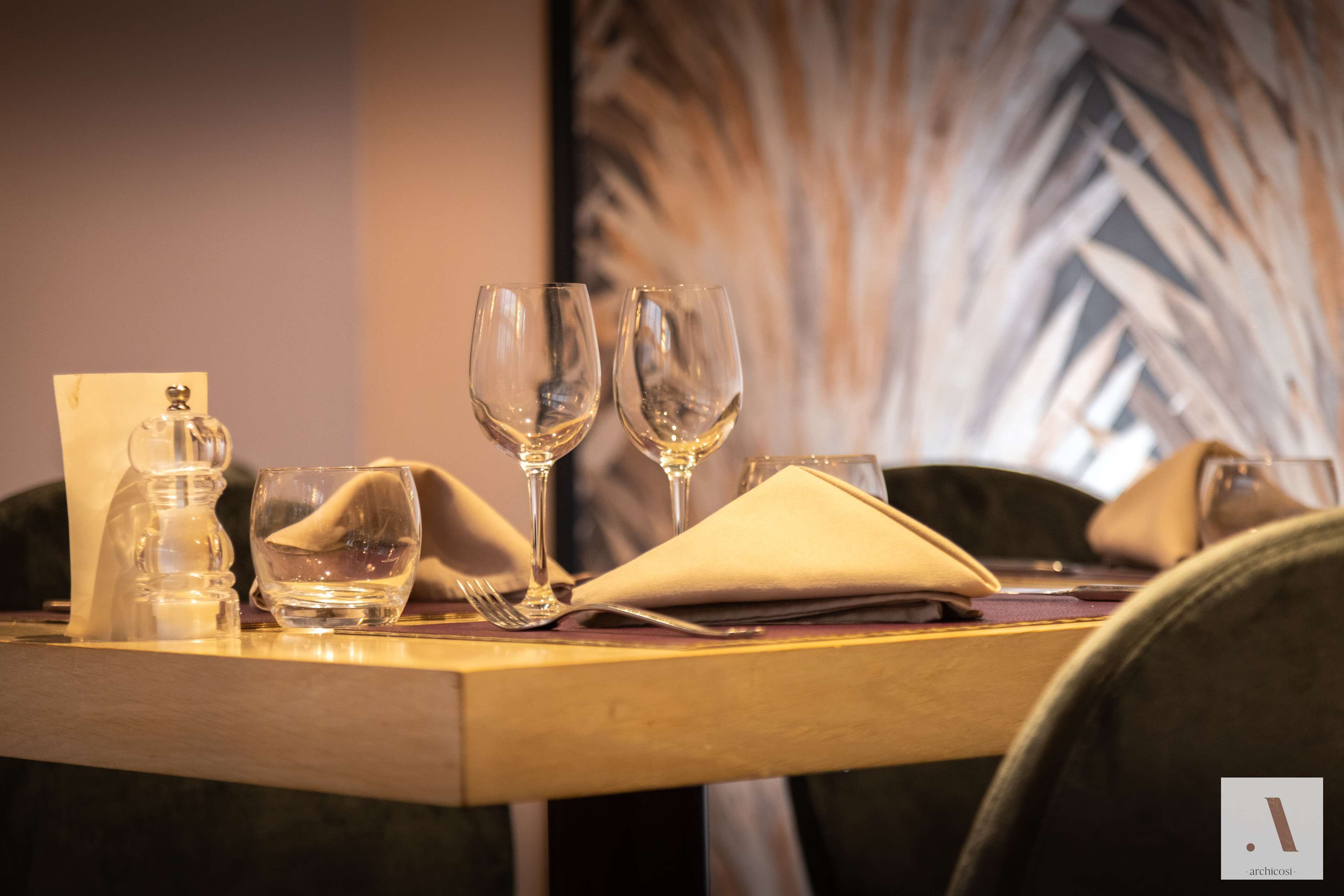A dining table set with a water bottle, two wine glasses, a folded napkin, and a menu.