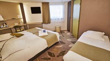 A hotel room with two beds, a desk with a chair, a flat-screen TV, a window with curtains, and a carpet with a leaf pattern.