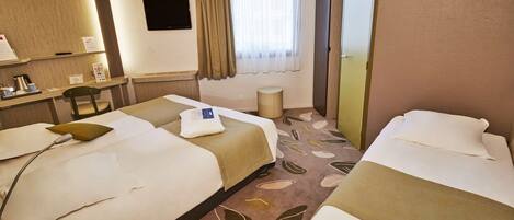 Habitación de hotel con dos camas, un escritorio con una silla, un televisor de pantalla plana, una ventana con cortinas y una alfombra estampada con hojas.
