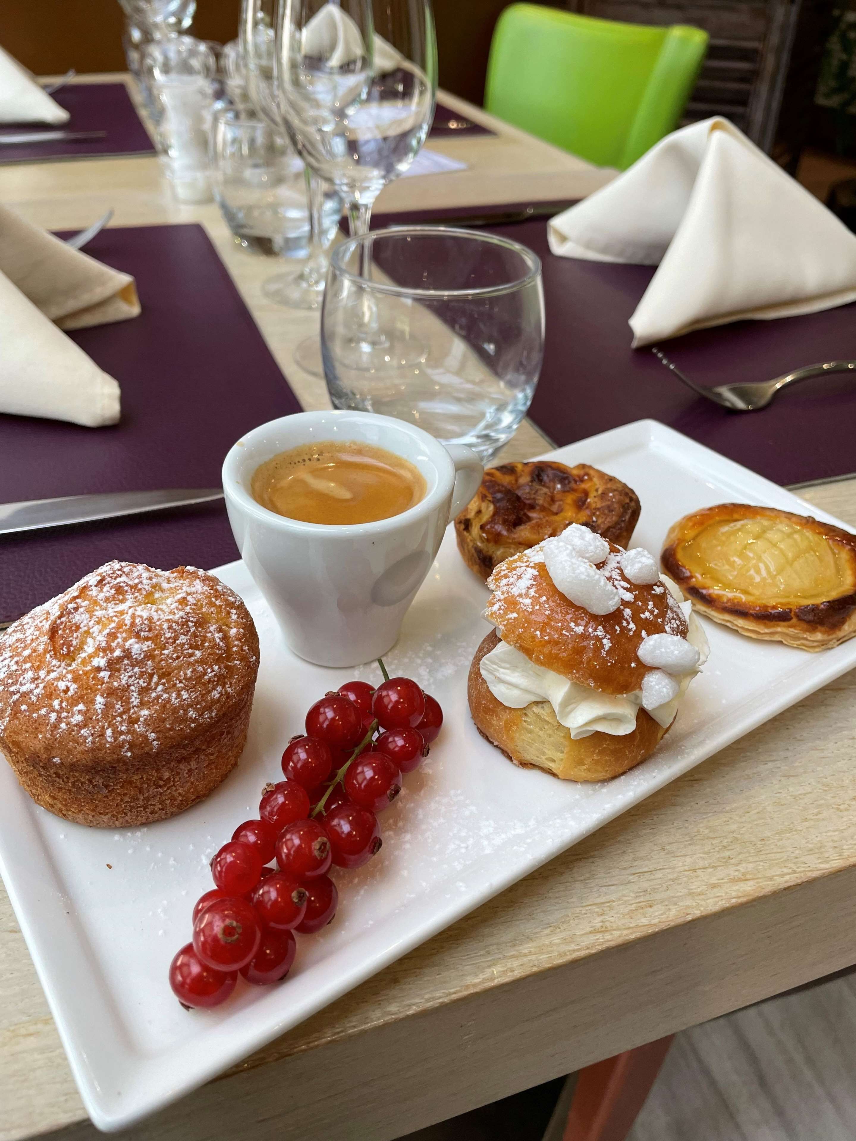 A dining table with a plate of pastries, a cup of coffee, and a glass of water.