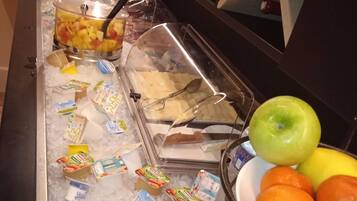 Un bufé con diversas opciones de comida, incluyendo frutas, yogur y un plato con trozos de piña.
