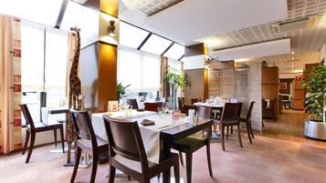 Comedor con mesas dispuestas para dos, con sillas de madera oscura y manteles blancos.