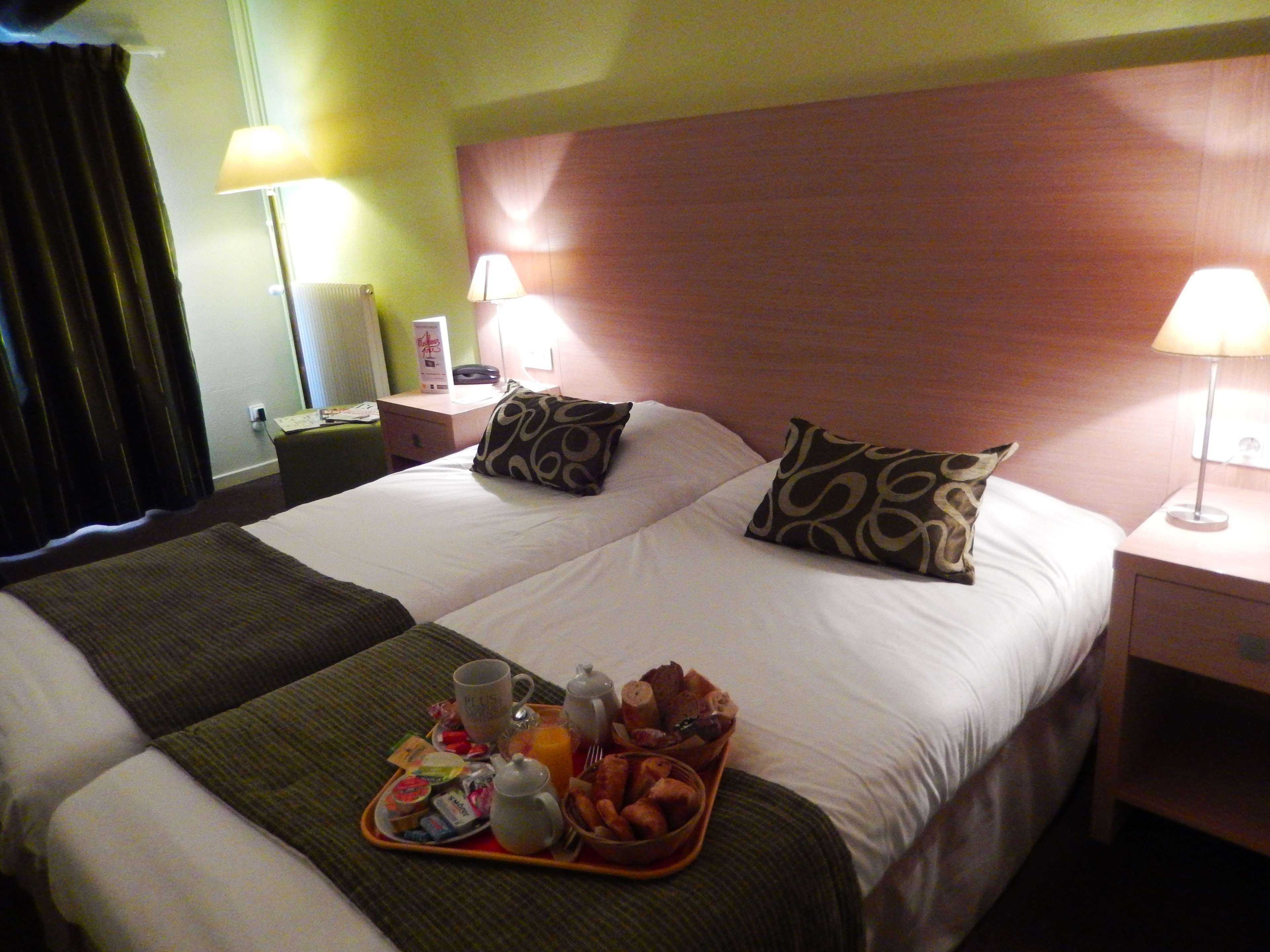 A hotel room with two beds, a tray with breakfast items, and bedside lamps.