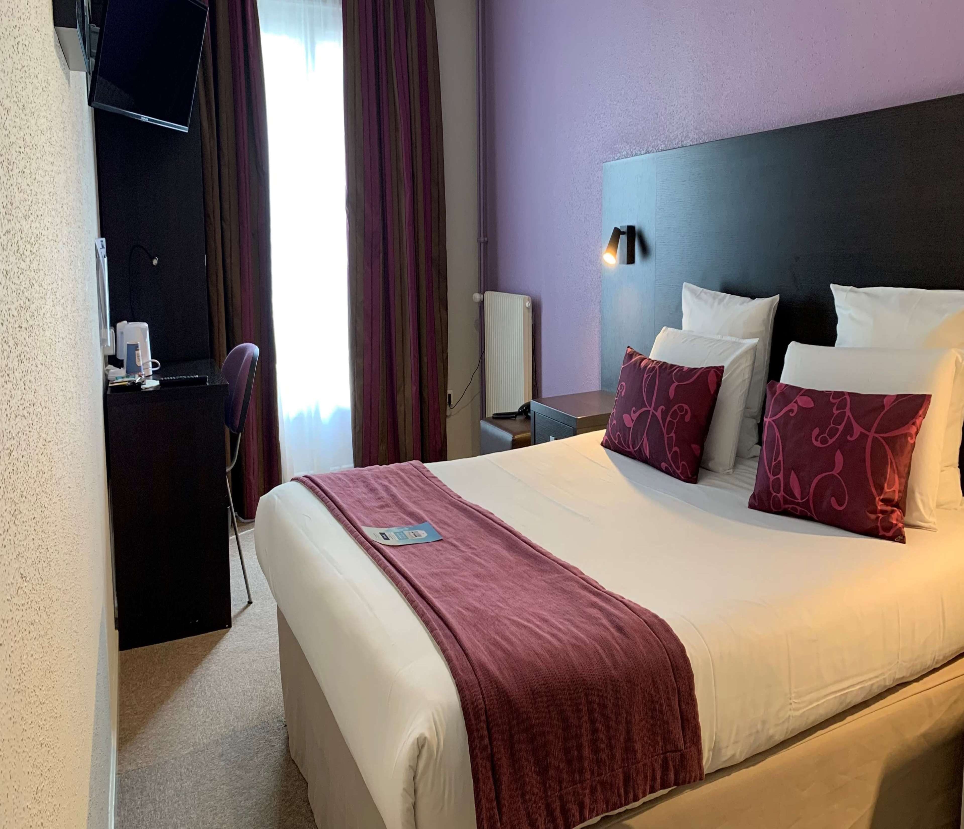 Ein Hotelzimmer mit einem Bett, einem Schreibtisch, einem Stuhl, einer Lampe und einem Vorhangfenster.
