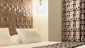 Habitación de hotel con pared de textura de madera, lámpara colgante de diseño geométrico, colcha estampada y cortina con diseño.