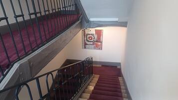 Un escalier dont les marches sont recouvertes d’une moquette rouge et dont les rampes sont noires, menant à un palier orné d’un tableau abstrait aux couleurs rouge et blanche.