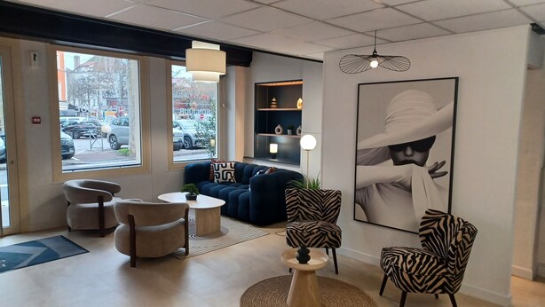 Un hall moderno de hotel con un sofá, sillones, una mesa de centro y una obra de arte grande enmarcada en la pared.