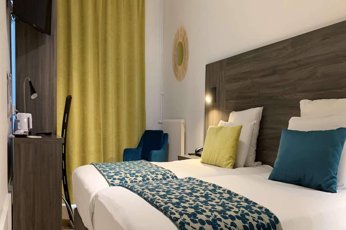 Ein Hotelzimmer mit einem großen Bett, einem Schreibtisch mit Stuhl, einem Telefon und einem gelben Vorhang.