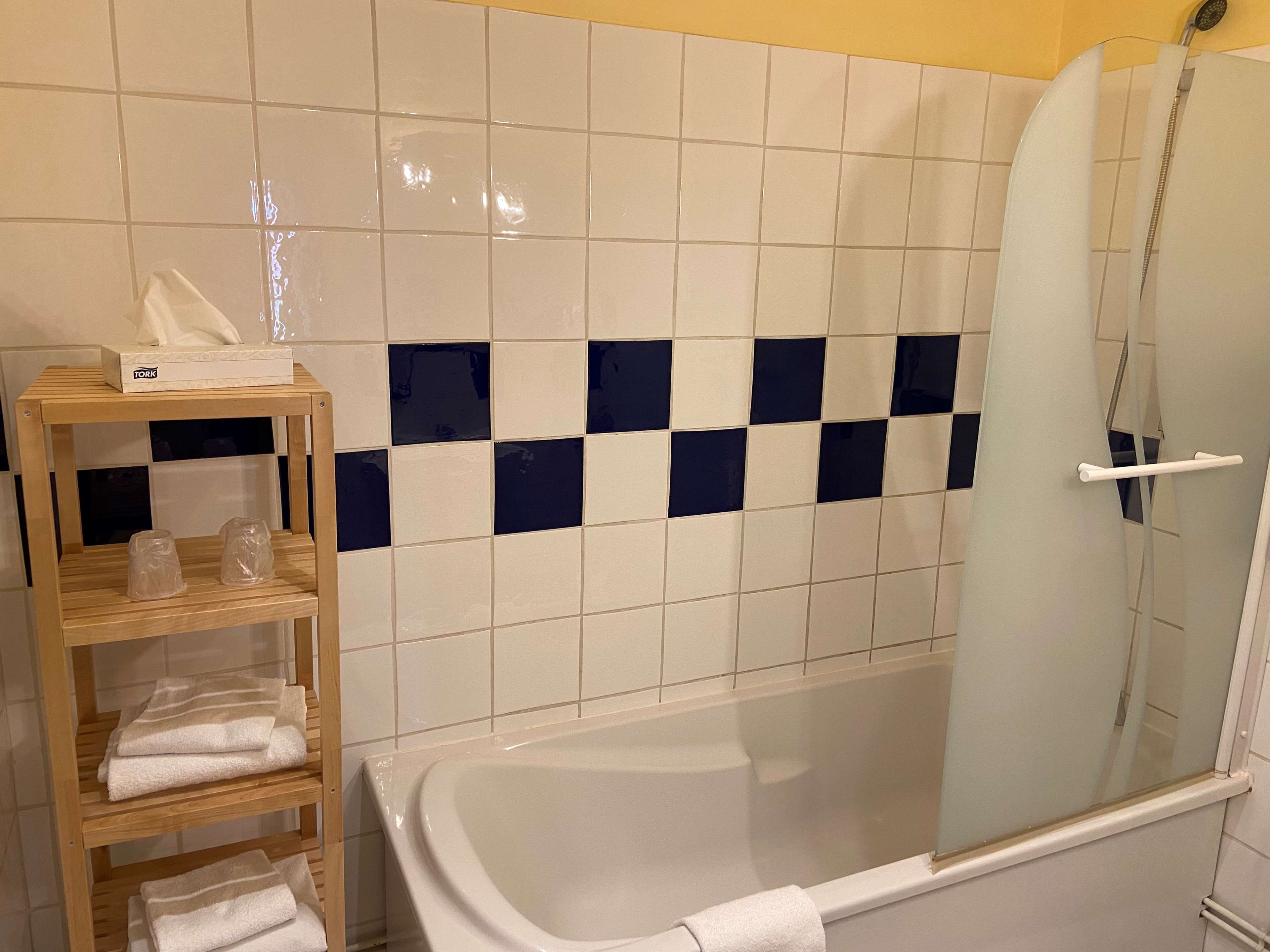 Un baño con bañera, cabina de ducha de cristal y estante de madera con toallas.