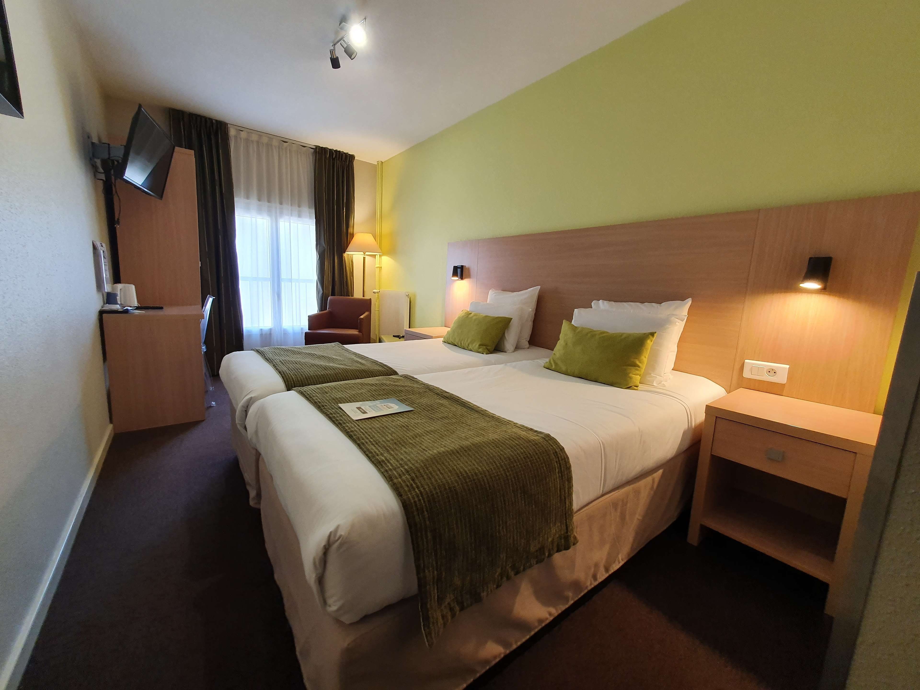 Ein Hotelzimmer mit einem großen Bett, Nachttischen, einem Schreibtisch, einem Sessel, einer Lampe und einem Fernseher.