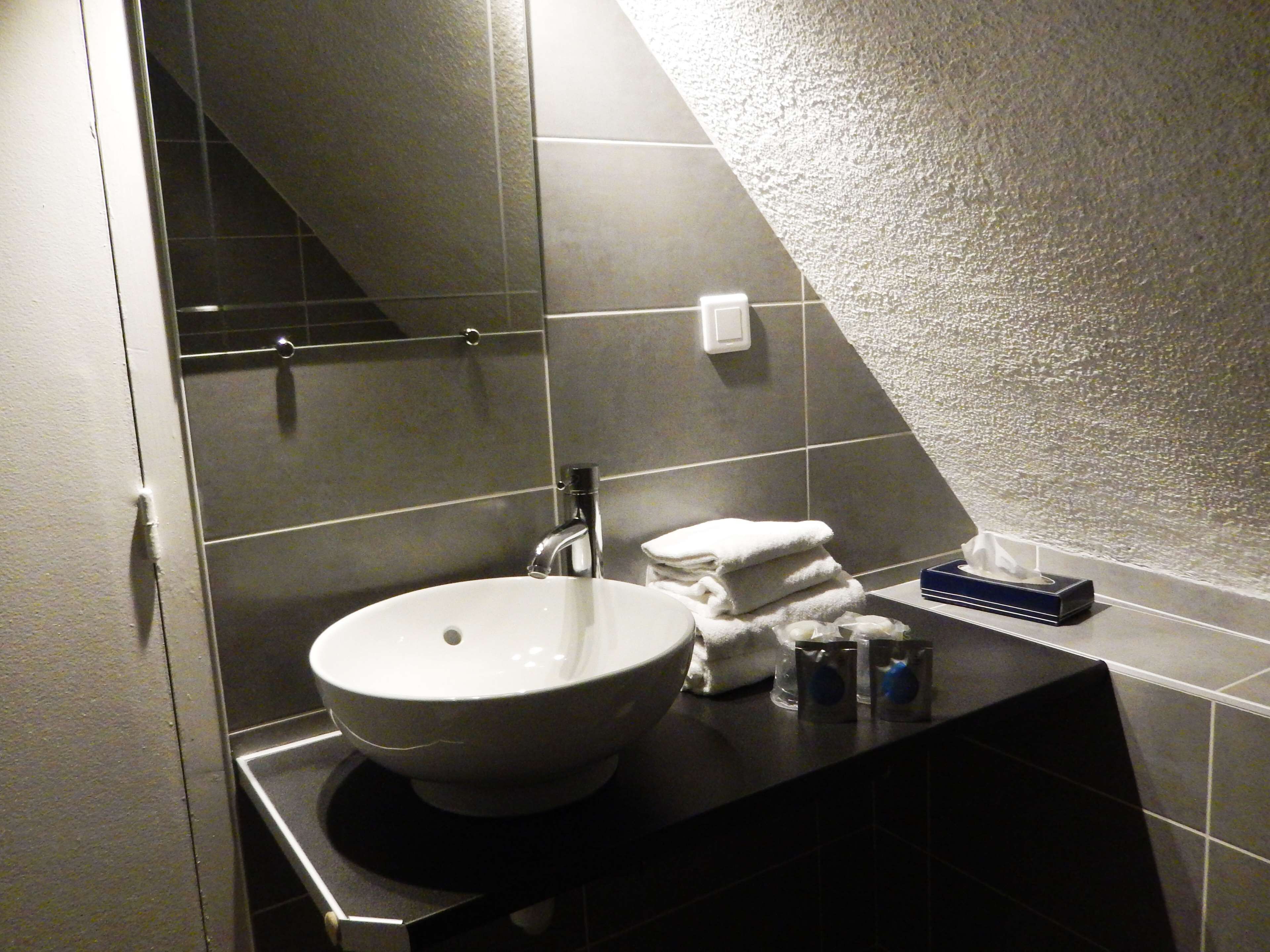 A bathroom with a white sink, dark tiles, and a towel rack.