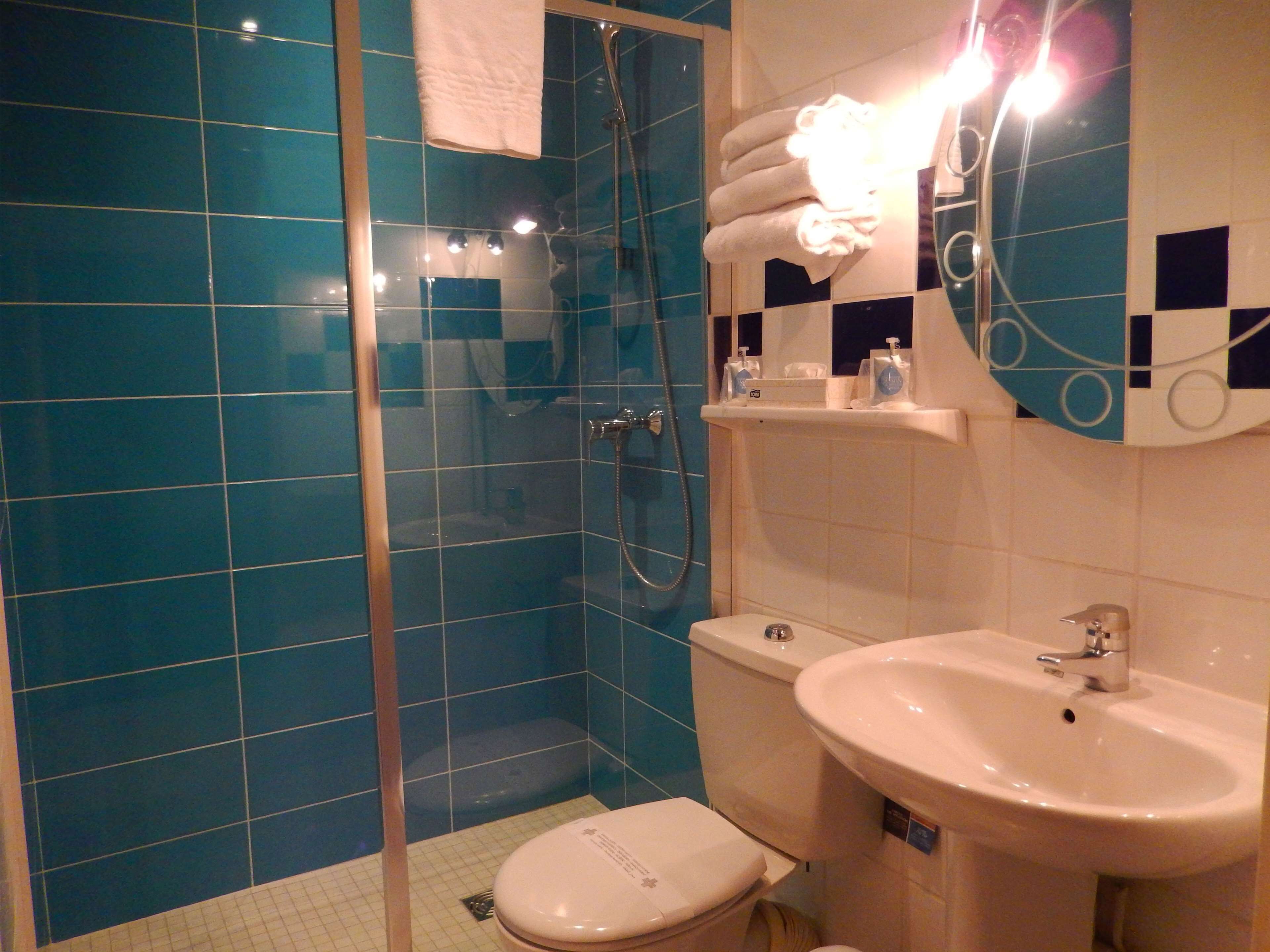 Een badkamer met blauwe tegels, een douchecabine van glas, een toilet en een wastafel.