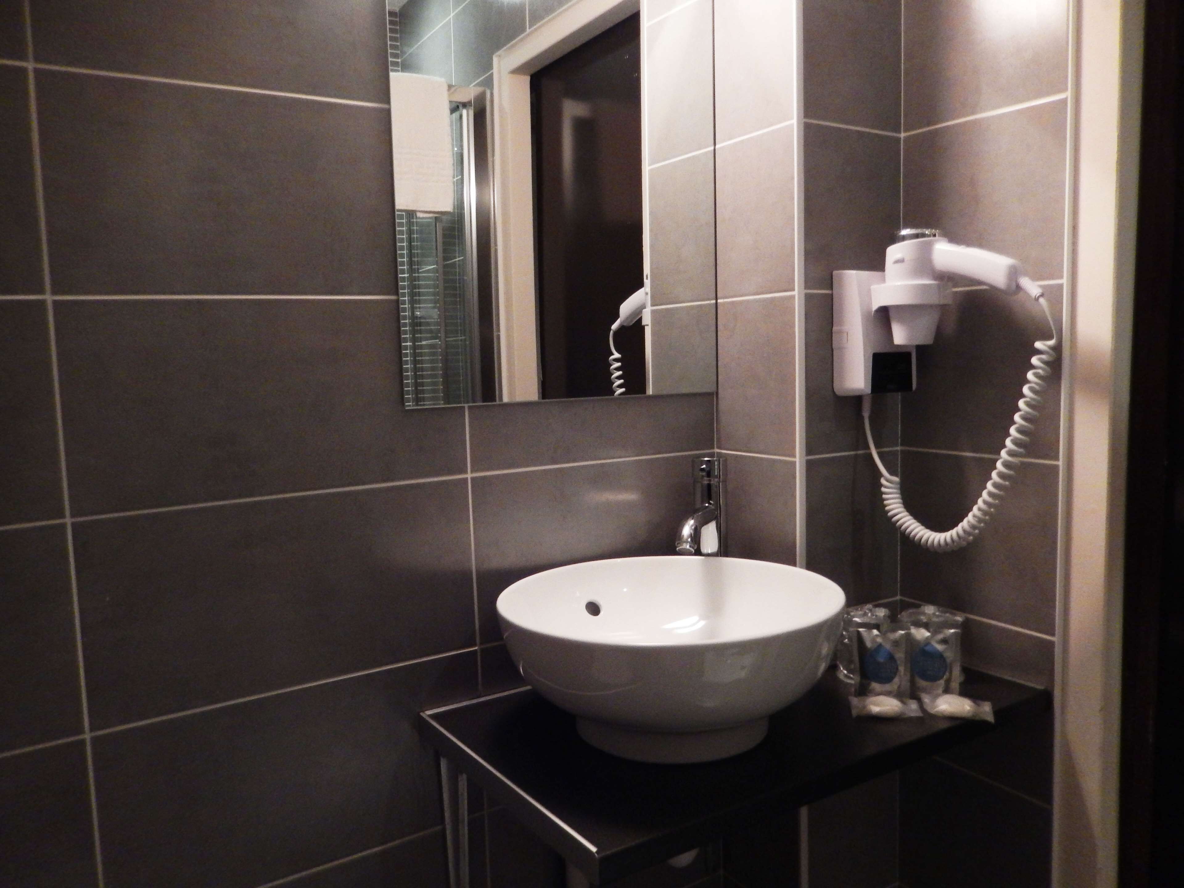 A bathroom with a white sink, a mirror, a hairdryer, and a towel dispenser.