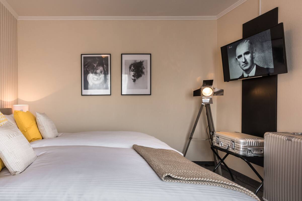 A hotel room with a large bed, two framed pictures on the wall, a television, and a lamp.