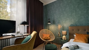 Une chambre d’hôtel avec un lit, un bureau équipé d’un ordinateur, une chaise, une lampe et une fenêtre avec des rideaux.