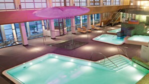 Un espace piscine intérieur moderne comprenant plusieurs bassins, des chaises longues et un espace de détente abrité.