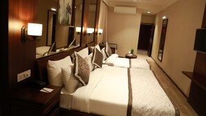 Habitación de hotel con una cama grande, una mesita de noche con lámpara, un espejo y una pequeña mesa con una planta.