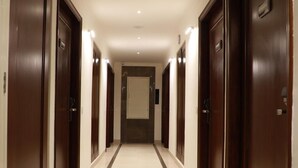 Un pasillo de hotel con puertas de madera oscura, piso de baldosas e iluminación empotrada.